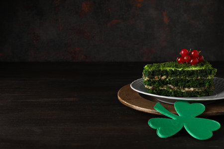 Piece of cake on plate and clover leaf on dark background, space for textの写真素材