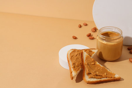 Peanut paste in a glass jar with toast, on a light background.