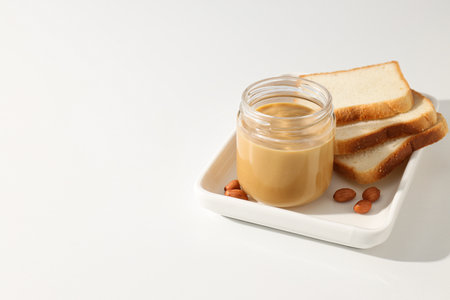 Peanut paste in a glass jar with toast, on a light background.