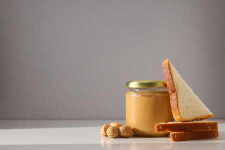 Peanut paste in a glass jar with toast, on a light background.