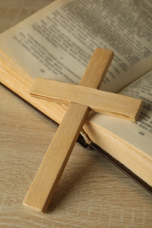 Wooden cross on book on wooden background, close up