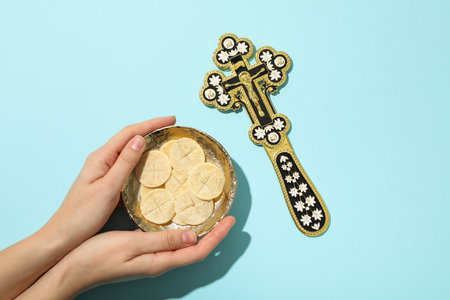 Bread in bowl in hands and cross on blue background, top view