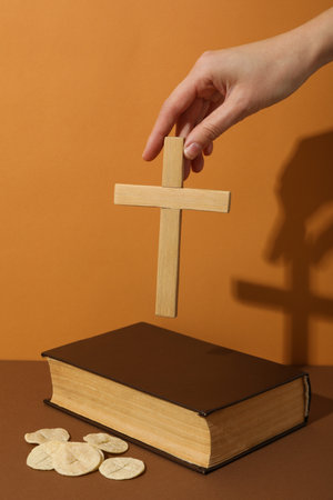 Bread, wooden cross in hand and Bible on orange backgroundの写真素材