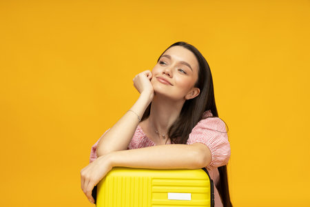 Happy young girl with a suitcase on a yellow backgroundの写真素材