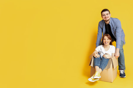 A couple with boxes, on a yellow background, the concept of moving.の写真素材