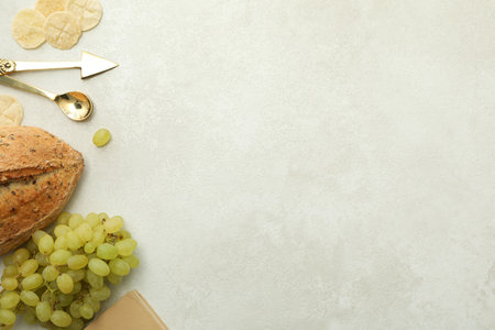 Bread, grapes, book and cutlery on light background, space for text