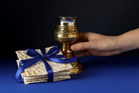 Matzo with ribbon and cup in hand on dark blue background
