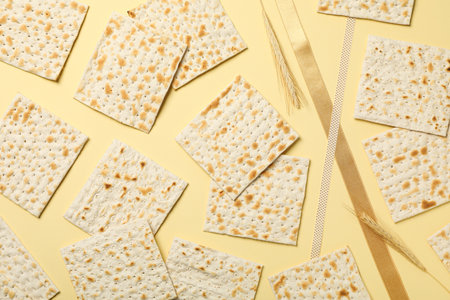 Matzo, spikelets and ribbons on light yellow background, top view