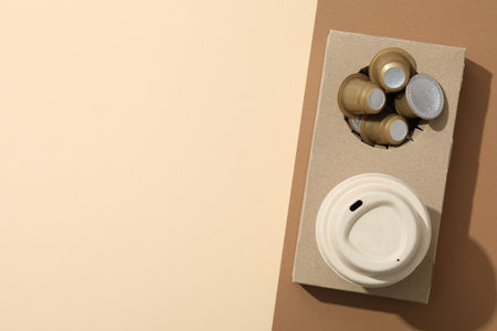 Coffee capsules and paper cup in paper stand on brown and beige background, space for textの写真素材