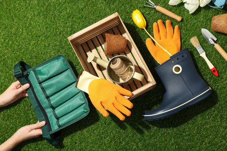Garden tools and supplies in hand on green background, top view