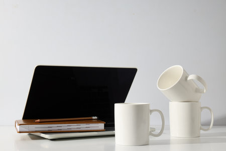 White cups on a table with a laptopの写真素材
