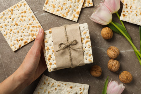 Matzo in hand, nuts and flowers on gray background, top view