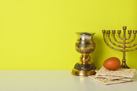Matzo, egg, cup and hanukkiah on yellow background, space for text