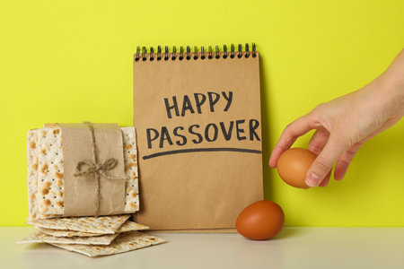 Matzo, egg in hand and notepad with text on yellow background