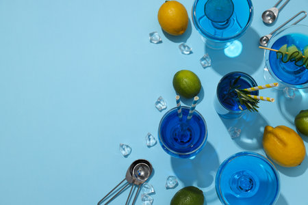 Blue drink in cocktail glasses, lemons, limes and ice cubes on blue background, space for textの写真素材