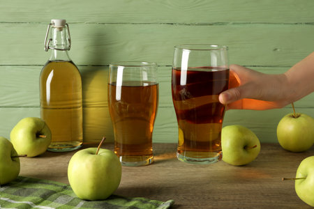 Glasses and bottle with apple cider, hand and green apples on table on wooden green backgroundの写真素材