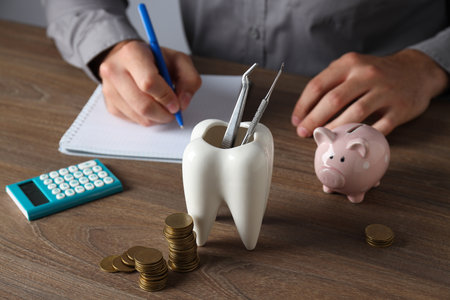 Tooth with dental instruments, piggy bank, calculator, coins and hands on table on gray backgroundの写真素材