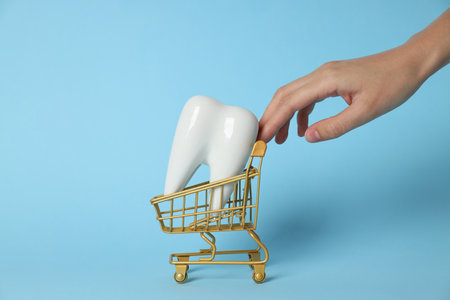 Tooth in shopping cart and hand on blue background