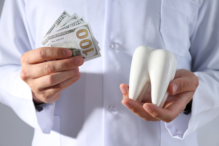 Dollars and tooth in hands of dentist on gray backgroundの写真素材