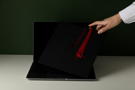 A graduate's hat on a laptop, on a green background.の写真素材