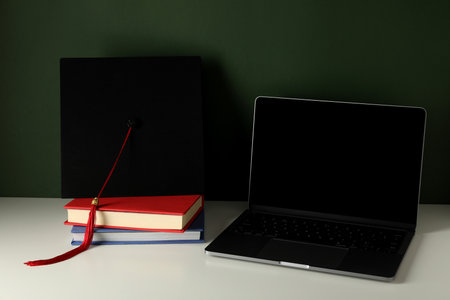 A graduate's hat on a laptop, on a green background.の写真素材