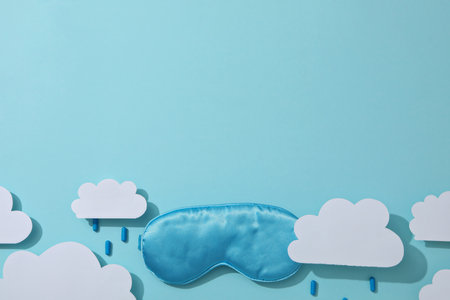 Sleep mask, pills and paper clouds on blue background, space for textの写真素材