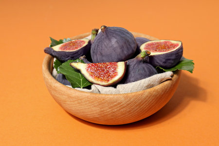 Fresh ripe figs in a wooden bowl on an orange backgroundの写真素材