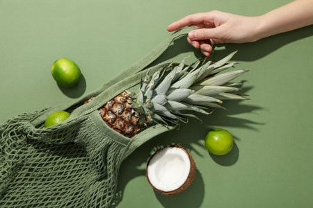 Bag with tropical fruits in hand on green background, top view