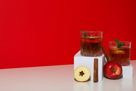Glasses with apple cider, apples and cinnamon sticks on red background, space for textの写真素材