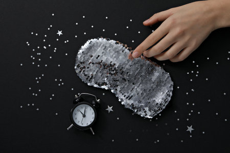 Sleep mask, alarm clock and hand on black background, top viewの写真素材