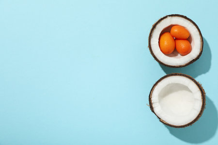Two half of coconut and whole kumquat on blue background, space for textの写真素材