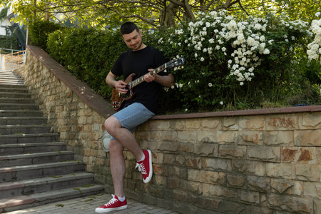 Attractive young guy playing guitar in the park