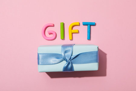 The word gift is made of colored plasticine, laid out on a pink background.