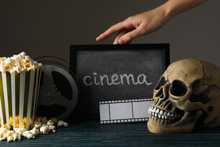 Blackboard, hand, skull, reel and paper cup with popcorn on dark backgroundの写真素材