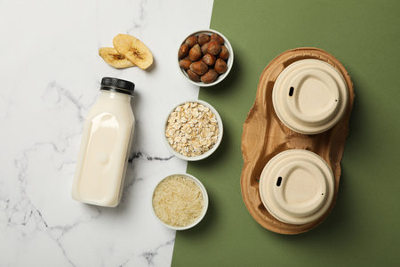 Bottle of alternative milk, herbal ingredients and paper cups on white and green background, top viewの写真素材