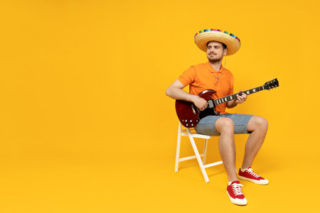 Attractive young guy playing guitar in Mexican hatの写真素材