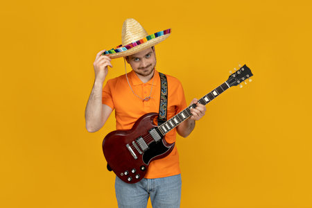 Attractive young guy playing guitar in Mexican hatの写真素材