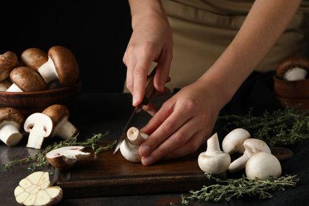 Fresh cut and whole champignons, bowls, kitchen board and knife in hand on dark backgroundの写真素材