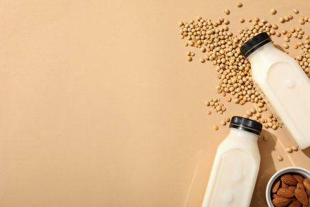 Bottles of milk, nuts in bowl, oatmeal and soy beans on beige background, space for textの写真素材