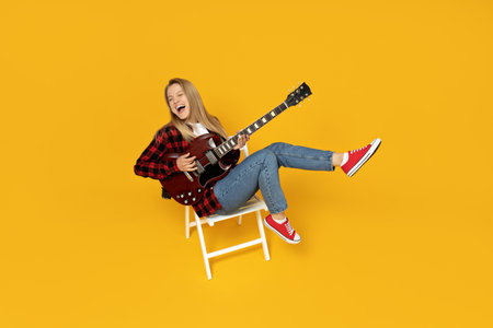 Attractive young girl playing the guitar on a yellow backgroundの写真素材