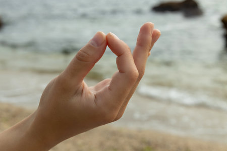 Fingers folded in zen sign on seashore, close upの写真素材