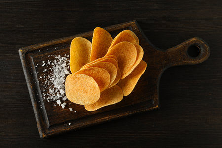 Potato chips on a wooden board with salt on a dark backgroundの写真素材