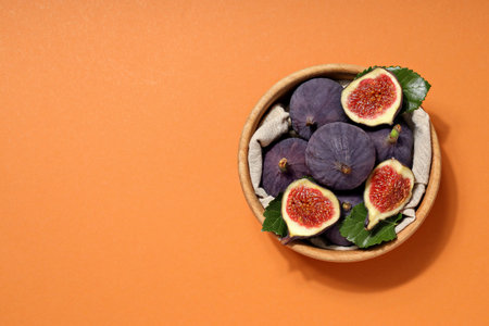 Fresh ripe figs in a wooden bowl on an orange backgroundの写真素材