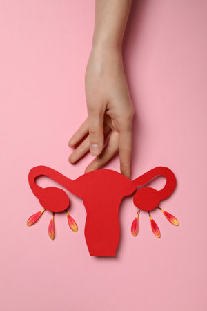 Red paper uterus and female hand on pink background, top view