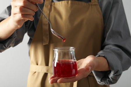 Jar of fig jam and spoon in hands on white background
