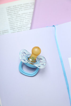 Open books with a baby pacifier on a pink background