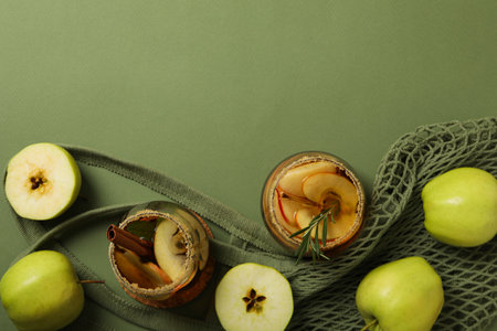 Glasses with apple cider and green apples on bag on green background, space for textの写真素材