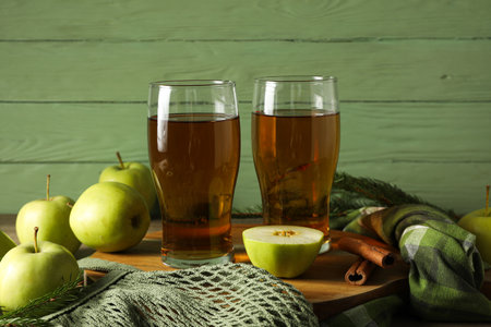 Glasses with apple cider, bag with green apples on wooden table on green wooden backgroundの写真素材