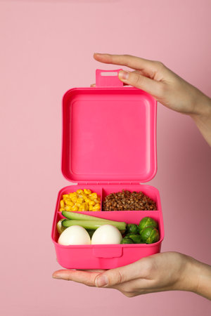 Pink lunch box in hands on pinkの写真素材