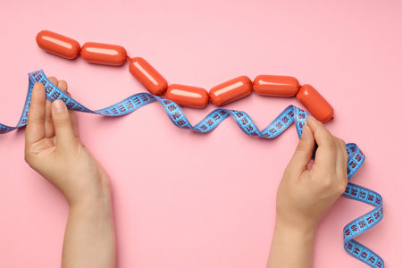Small sausages with a measuring tape on a pink backgroundの写真素材